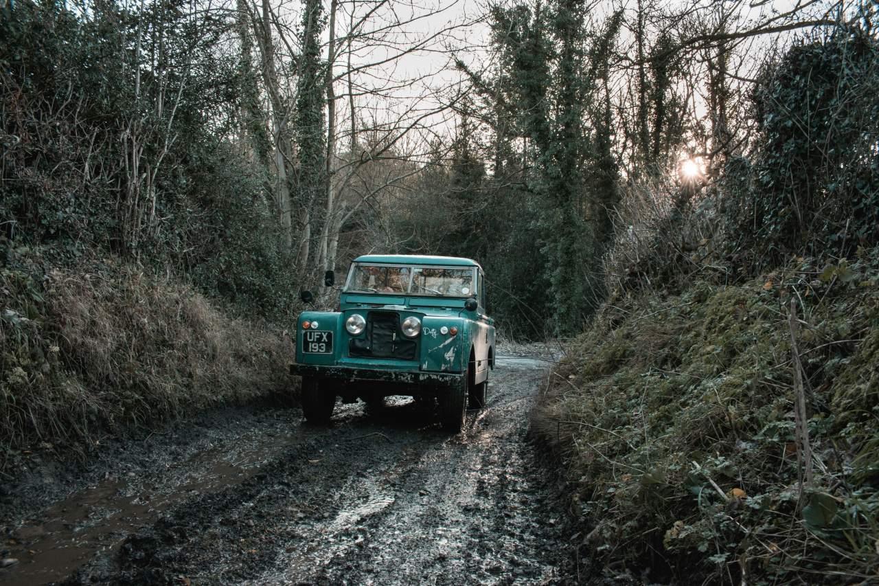 Old Land Rover driving up a muddy farm road.