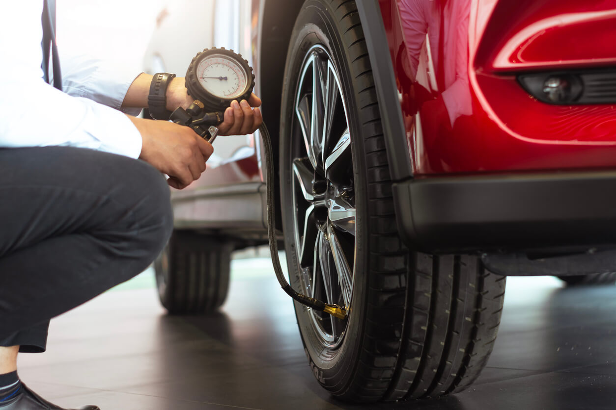 Person kneeling alongside their car checking the pressure of a tyre.
