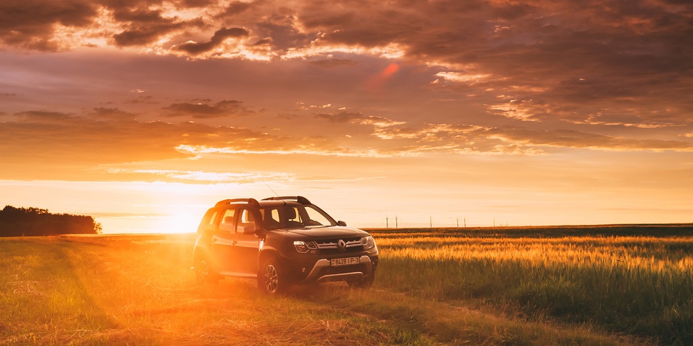 An SUV parked in the grass with sunset in the background.