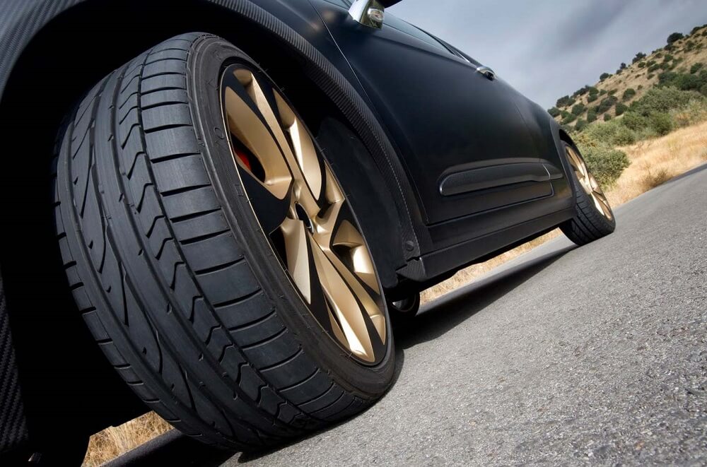 A black car is parked on the side of the road with sporty wheels and tyres.