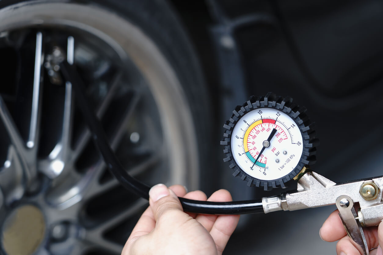 Holding a tyre pressure gauge with a wheel and deflated tyre tyre in the background