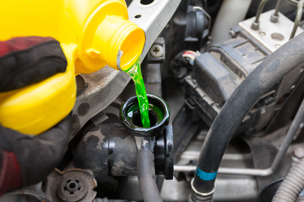 Person pouring green anti-freeze coolant additive into radiator cap