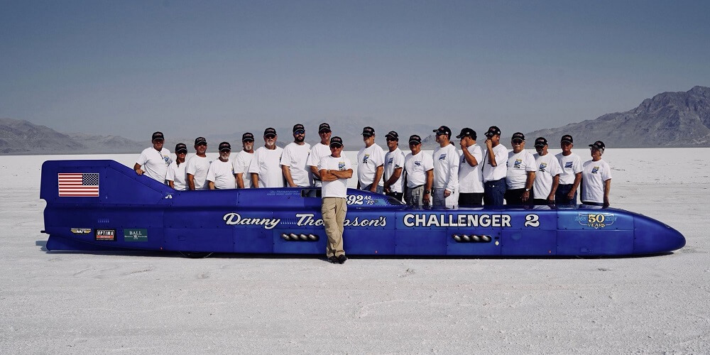 A team of racing experts stand with the blue challenger 2 vehicle after setting a new land speed record for the fastest naturally aspirated vehicle.