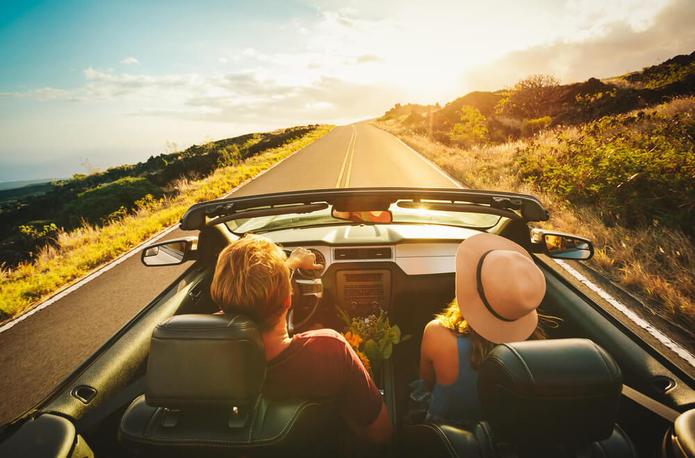 Two people driving in a convertible on a hot summer day.