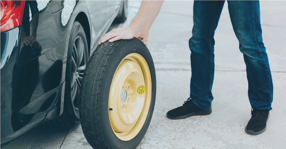 A man pushes a yellow space saving spare tyre towards the vehicle.