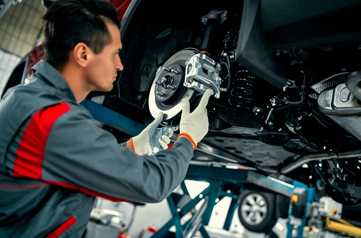 A car mechanic repairs the suspension of a lifted car at an auto repair shop.