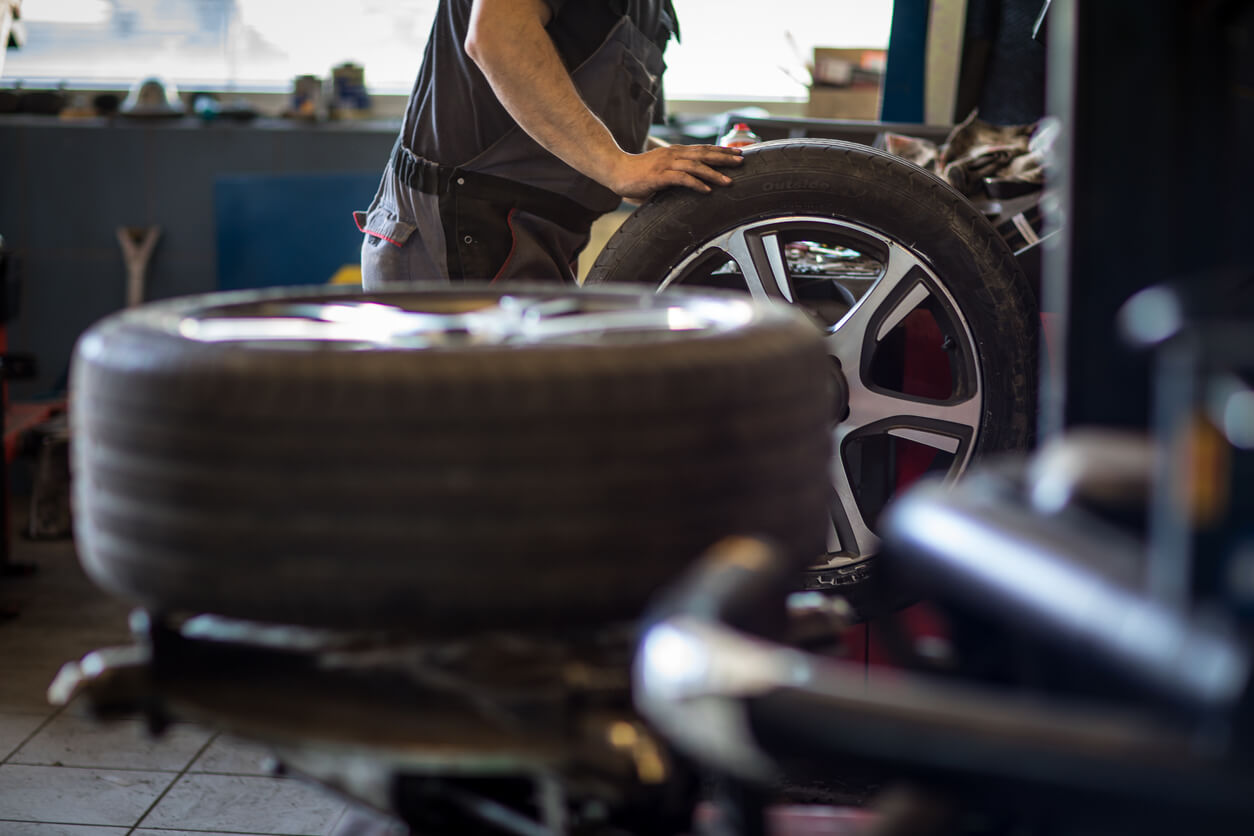 Technician in a workshop with a new car tyre and wheel.